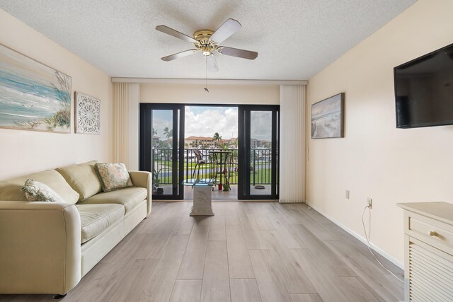 living room featuring ceiling fan, light wood-type flooring, and a textured ceiling