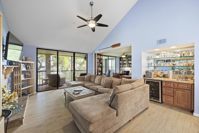 living room with beverage cooler, ceiling fan, light hardwood / wood-style flooring, wet bar, and a high ceiling