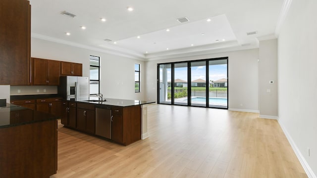 kitchen featuring a kitchen island with sink, a raised ceiling, sink, light wood-type flooring, and appliances with stainless steel finishes