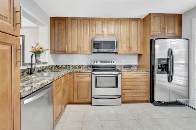 kitchen with appliances with stainless steel finishes, light tile patterned flooring, light stone countertops, and sink