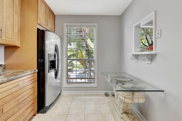 kitchen with light tile patterned floors, stainless steel fridge with ice dispenser, and light stone counters