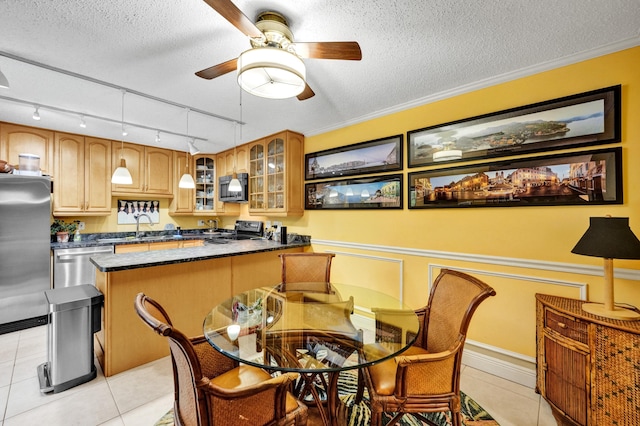 tiled dining space featuring ceiling fan, sink, track lighting, a textured ceiling, and ornamental molding