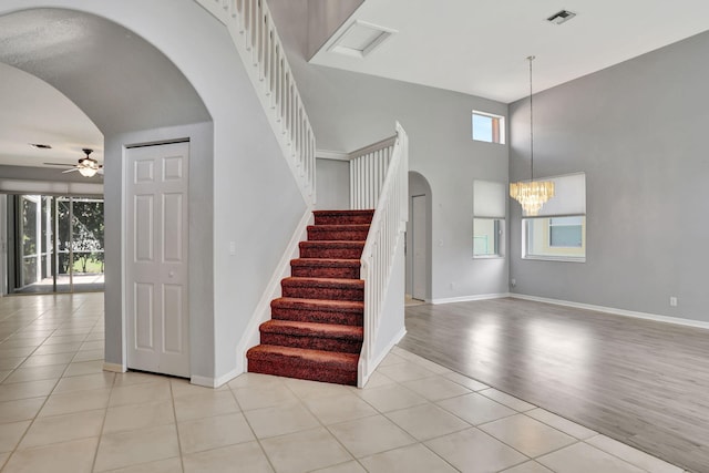 stairs featuring a high ceiling, hardwood / wood-style flooring, and ceiling fan with notable chandelier