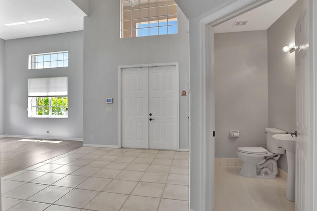 bathroom with a towering ceiling, toilet, and tile patterned floors