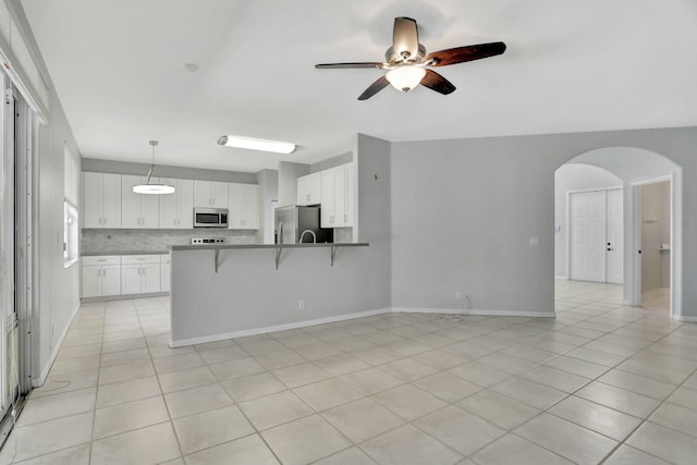 kitchen with appliances with stainless steel finishes, a kitchen bar, kitchen peninsula, white cabinetry, and decorative light fixtures