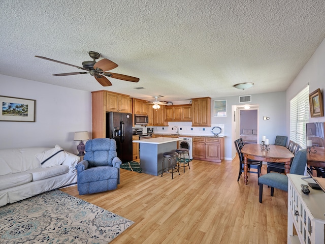 living room featuring sink, washer / clothes dryer, light wood-type flooring, a textured ceiling, and ceiling fan