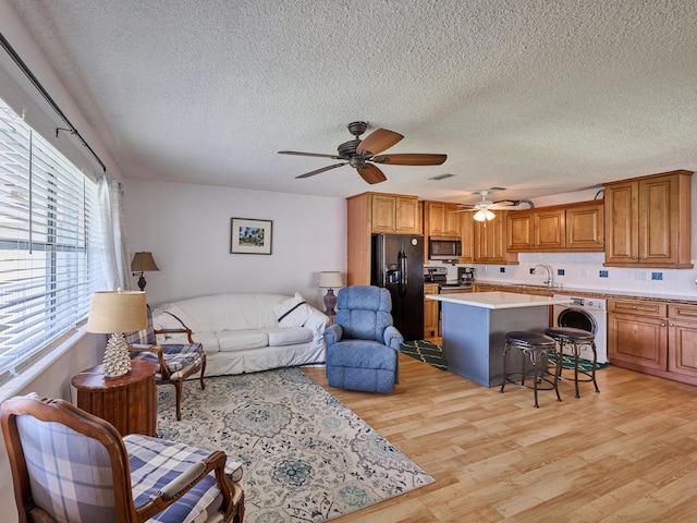 living room with ceiling fan, light wood-type flooring, sink, washer / clothes dryer, and a textured ceiling