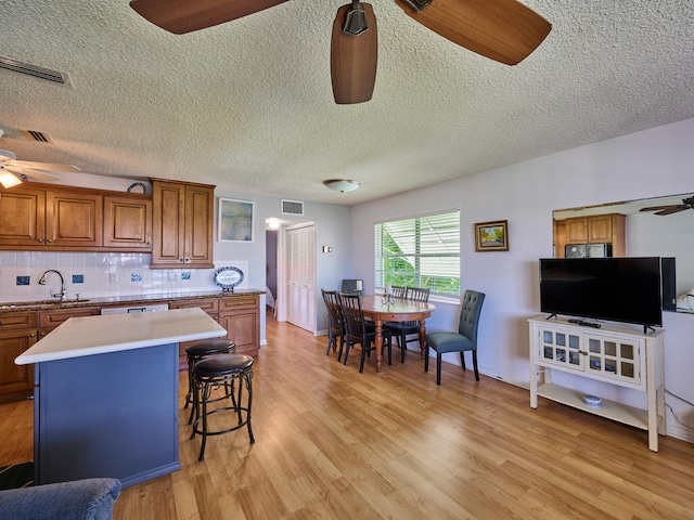 kitchen with ceiling fan, sink, a center island, light hardwood / wood-style flooring, and backsplash