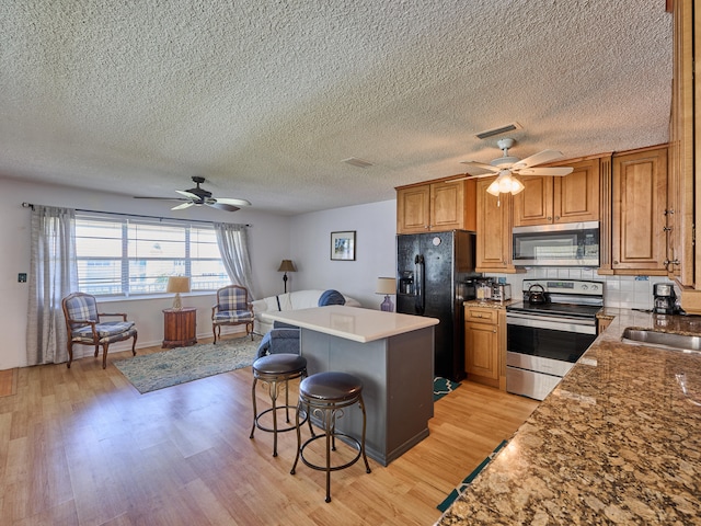 kitchen featuring a breakfast bar, appliances with stainless steel finishes, light wood-type flooring, and ceiling fan