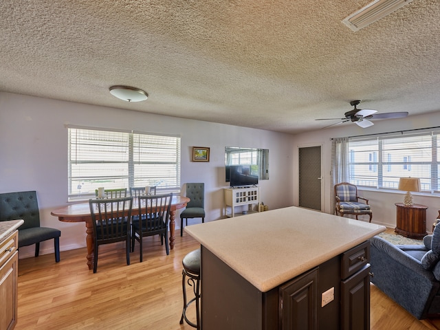 kitchen with a breakfast bar area, dark brown cabinets, light wood-type flooring, a center island, and ceiling fan