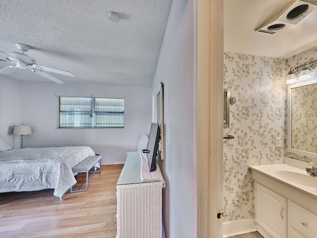 bedroom featuring a textured ceiling, sink, light wood-type flooring, and ceiling fan