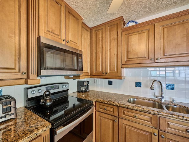 kitchen with dark stone counters, tasteful backsplash, sink, appliances with stainless steel finishes, and a textured ceiling