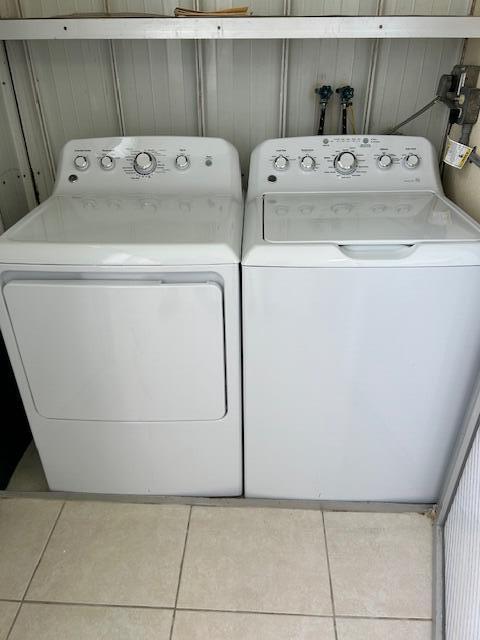 laundry room with light tile patterned floors, washer and clothes dryer, and wood walls