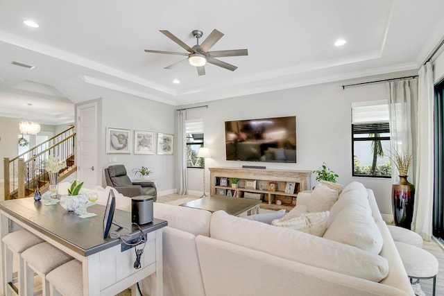 living room featuring light wood-type flooring, ceiling fan with notable chandelier, and a raised ceiling