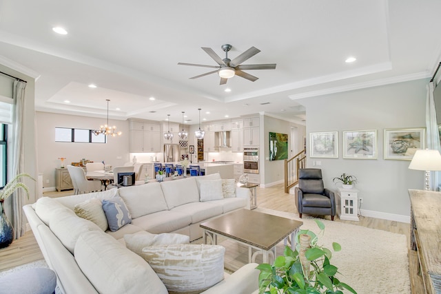 living room with ceiling fan with notable chandelier, a raised ceiling, ornamental molding, and light wood-type flooring