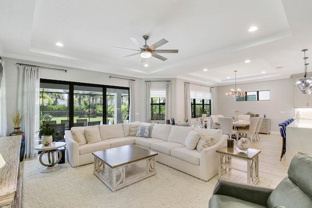 living room featuring a raised ceiling, ceiling fan with notable chandelier, and light hardwood / wood-style flooring