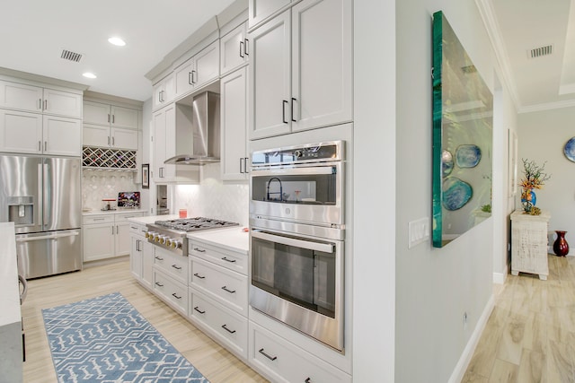 kitchen featuring crown molding, light hardwood / wood-style flooring, stainless steel appliances, and wall chimney range hood