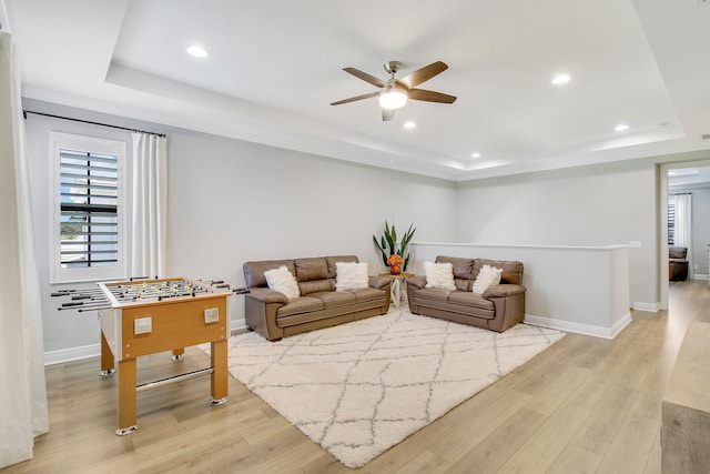 living room with light wood-type flooring, a tray ceiling, and ceiling fan