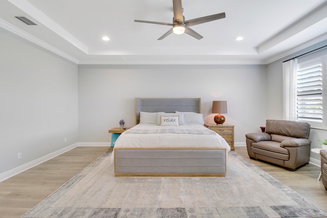 bedroom featuring light wood-type flooring, a raised ceiling, crown molding, and ceiling fan