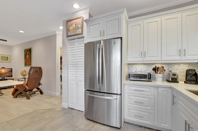 kitchen featuring crown molding, backsplash, white cabinets, and stainless steel fridge