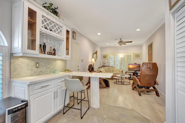 kitchen with crown molding, tasteful backsplash, white cabinetry, a breakfast bar, and ceiling fan