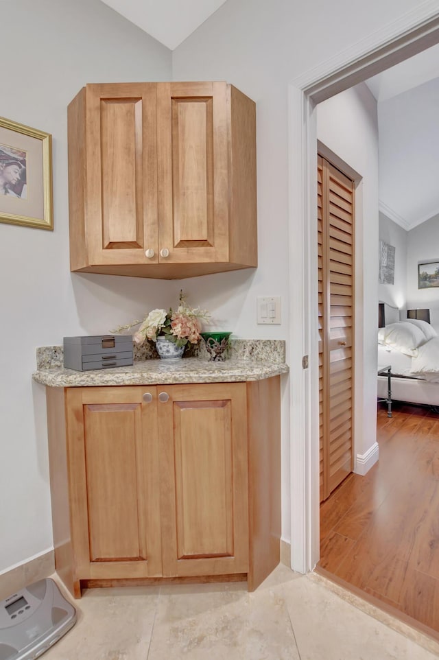 bar featuring light brown cabinets, light hardwood / wood-style flooring, and lofted ceiling