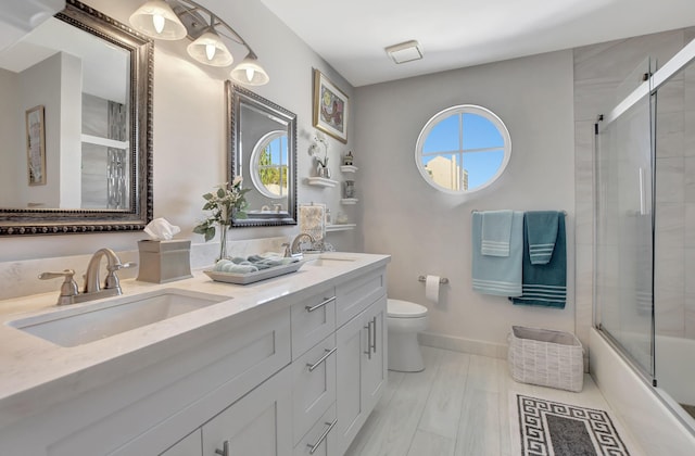 full bathroom with bath / shower combo with glass door, toilet, a wealth of natural light, and vanity