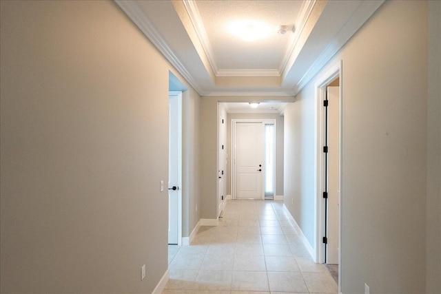 hall featuring light tile patterned flooring, ornamental molding, and a tray ceiling