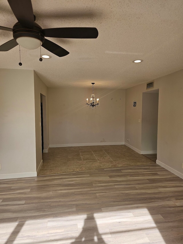 empty room featuring ceiling fan with notable chandelier, wood-type flooring, and a textured ceiling