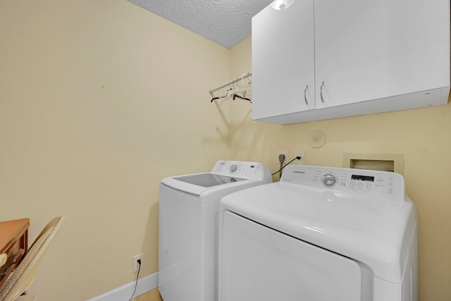 clothes washing area featuring washing machine and dryer, cabinets, and a textured ceiling