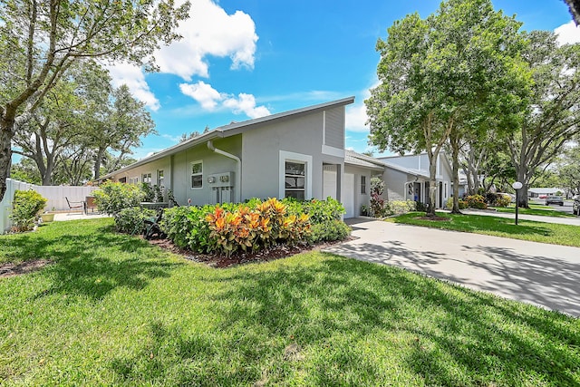 view of side of property featuring a yard, a garage, fence, stucco siding, and driveway