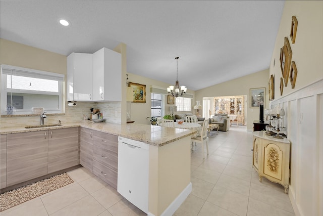 kitchen with light tile patterned floors, a peninsula, vaulted ceiling, a sink, and white dishwasher