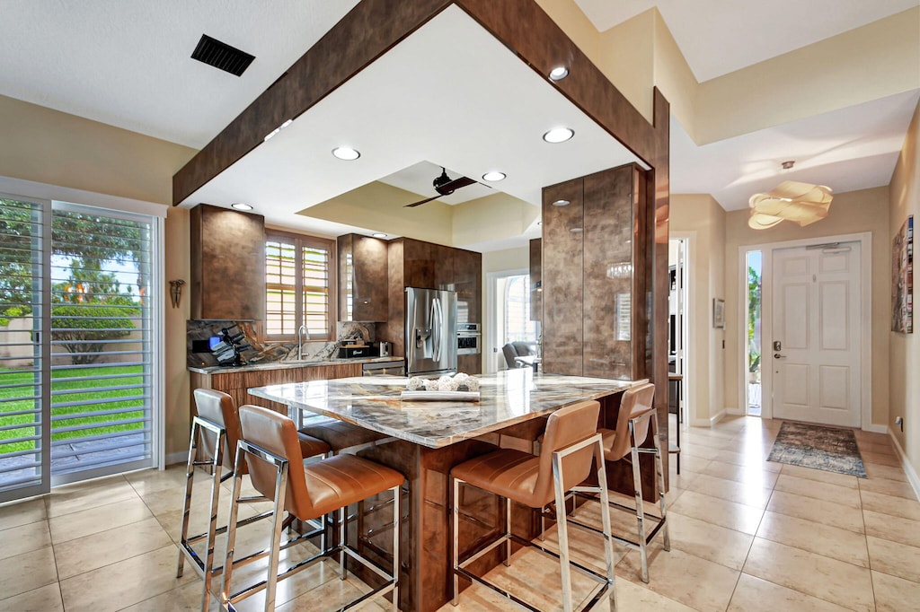 kitchen featuring dark brown cabinets, light tile patterned floors, stainless steel fridge, a center island, and a breakfast bar