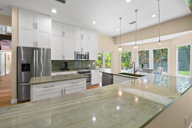 kitchen featuring appliances with stainless steel finishes, white cabinets, backsplash, hanging light fixtures, and light stone countertops