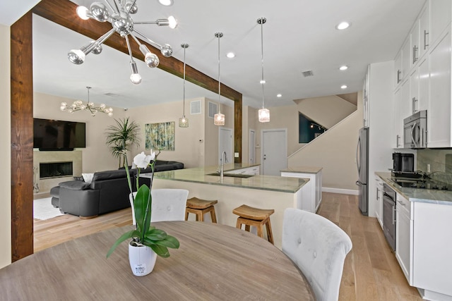 dining area featuring beamed ceiling, sink, a notable chandelier, and light wood-type flooring