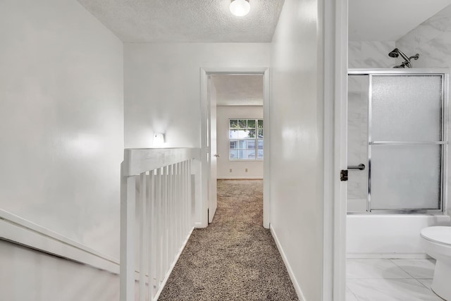 hall featuring a textured ceiling, carpet flooring, and baseboards