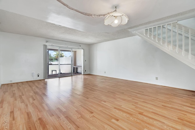 spare room featuring stairway, baseboards, a textured ceiling, and light wood finished floors