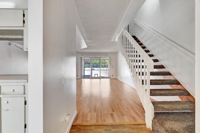 staircase featuring baseboards, a textured ceiling, and wood finished floors