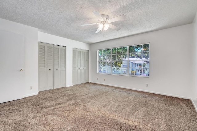 unfurnished bedroom with two closets, a textured ceiling, ceiling fan, and carpet flooring