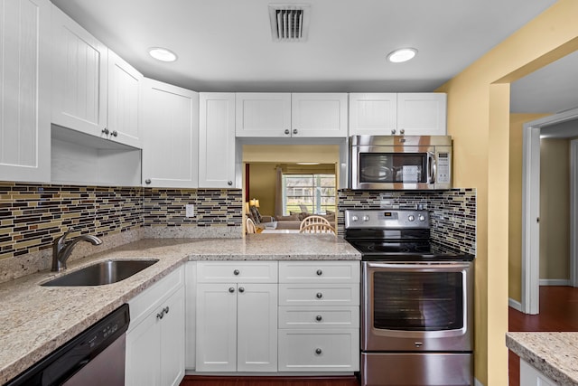 kitchen with stainless steel appliances, sink, light stone countertops, hardwood / wood-style flooring, and white cabinets