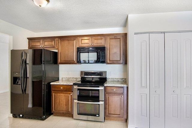 kitchen with black appliances, light tile patterned flooring, light stone counters, and a textured ceiling