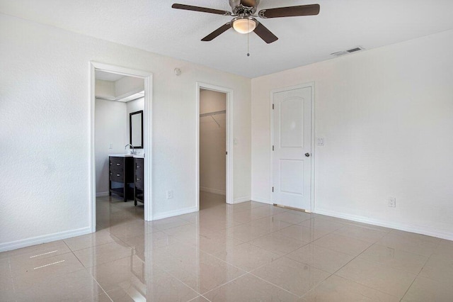 unfurnished bedroom featuring light tile patterned floors, a walk in closet, ensuite bathroom, and ceiling fan