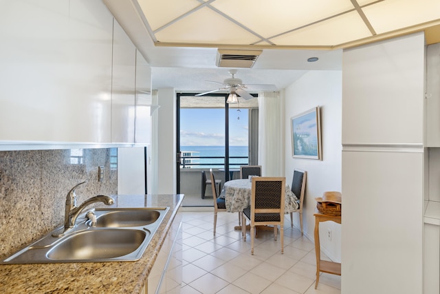 kitchen featuring ceiling fan, a water view, decorative backsplash, sink, and light tile patterned floors