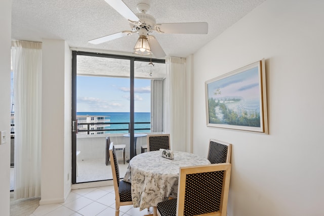 dining room with light tile patterned floors, a water view, a textured ceiling, and ceiling fan