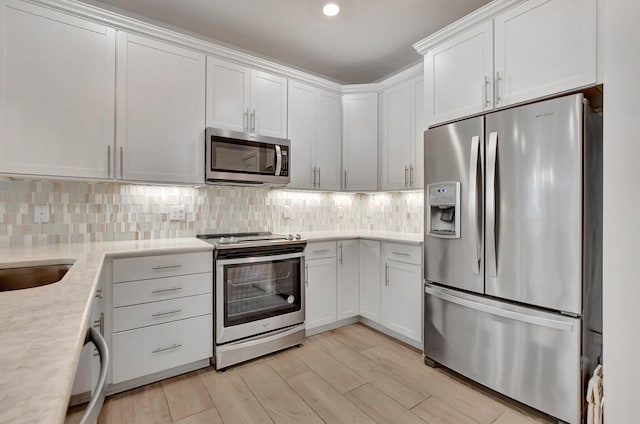 kitchen featuring white cabinets, appliances with stainless steel finishes, light hardwood / wood-style floors, and light stone counters