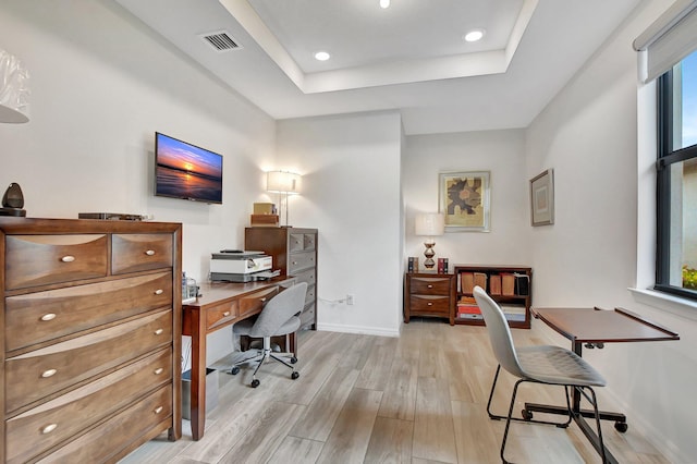 home office with light hardwood / wood-style floors and a tray ceiling