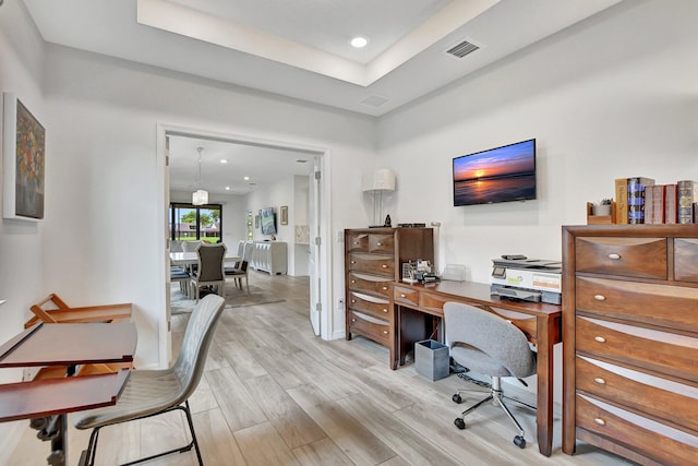 office space featuring a tray ceiling and light hardwood / wood-style flooring