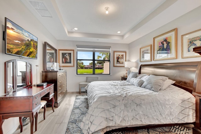 bedroom with a tray ceiling and light wood-type flooring