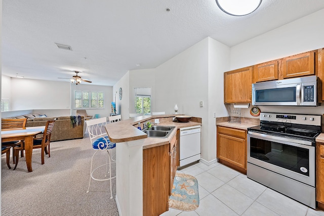 kitchen featuring ceiling fan, appliances with stainless steel finishes, sink, light tile patterned flooring, and a breakfast bar