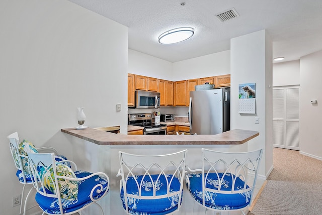 kitchen featuring light carpet, a textured ceiling, kitchen peninsula, and stainless steel appliances